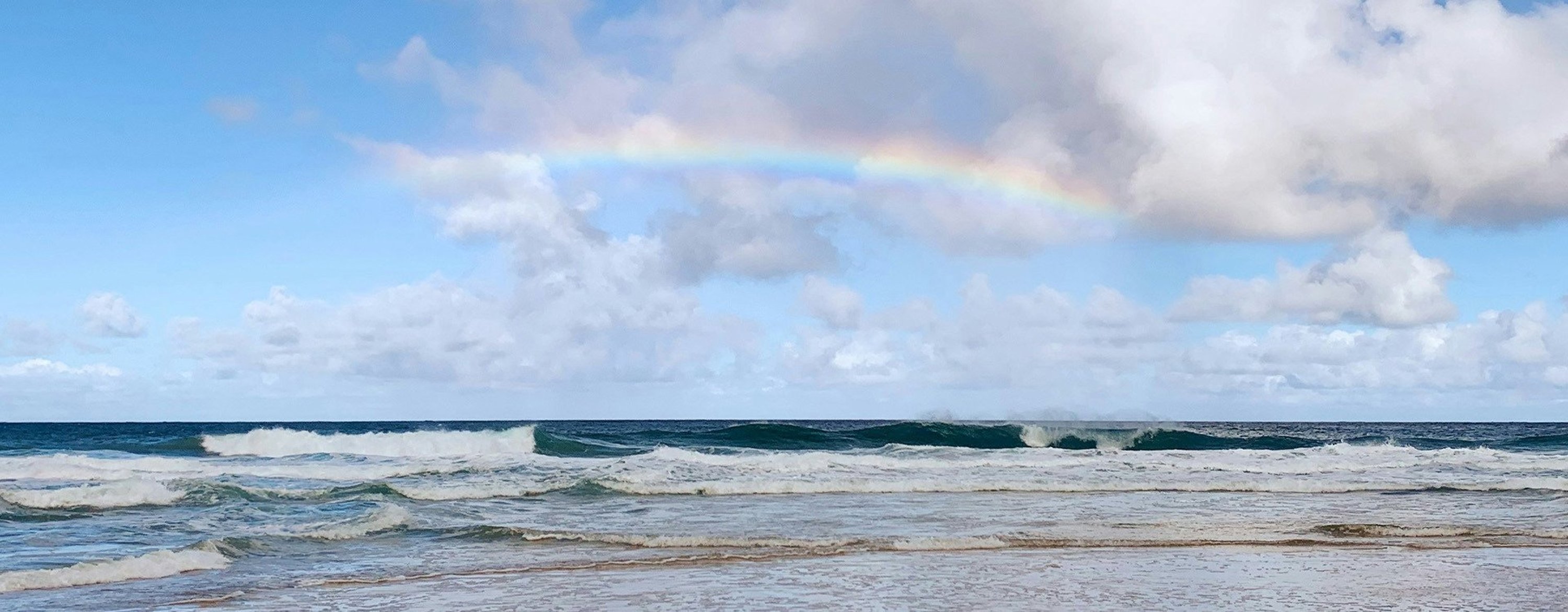 a rainbow forms above the breaking waves at the beach